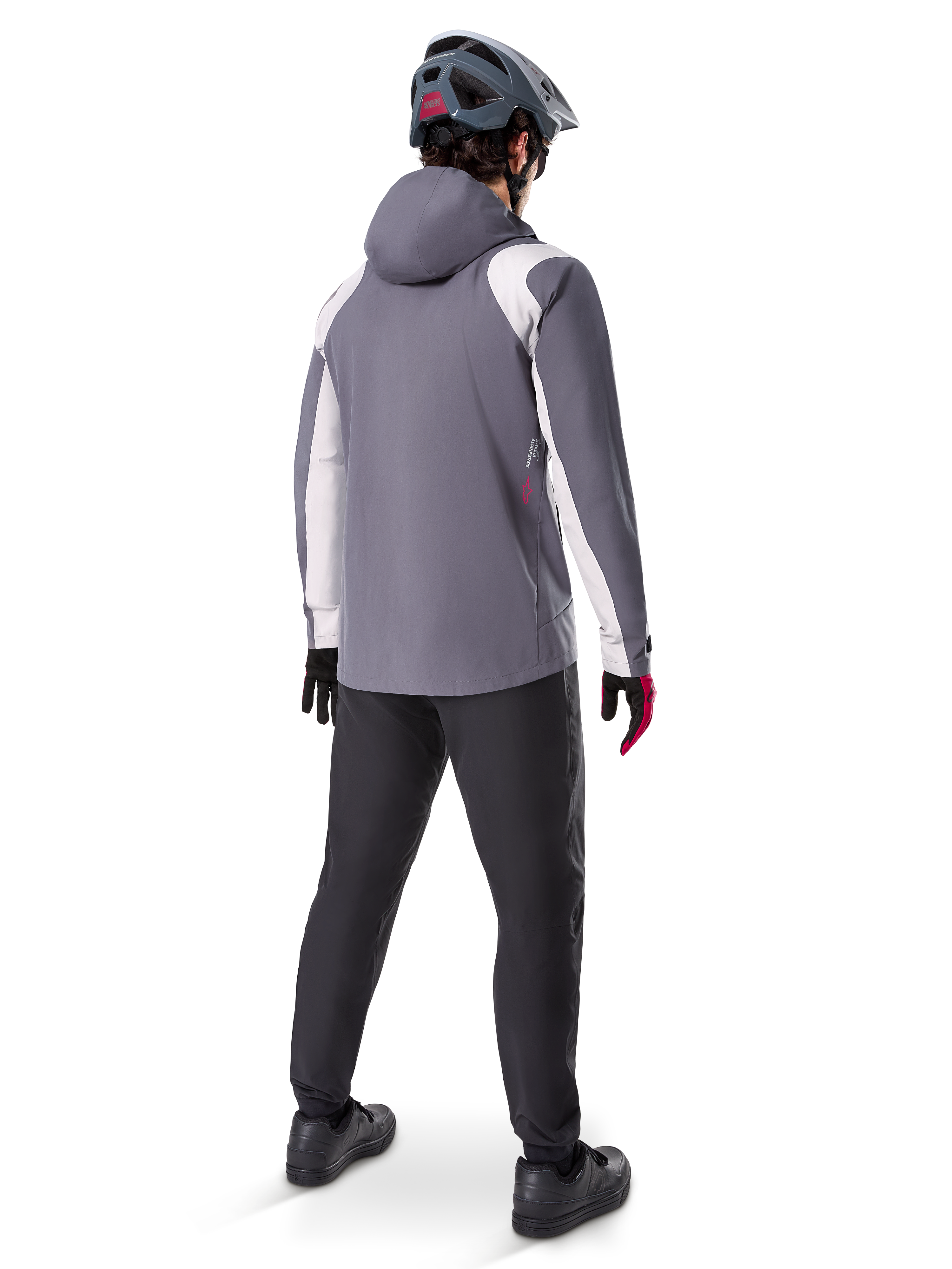 Alpinestars A-Dura Rain Jacket, chaqueta de ciclismo de montaña, gris titanio oscuro con paneles blancos, vista trasera de un ciclista con casco gris a juego y pantalones negros, equipamiento técnico para climas húmedos