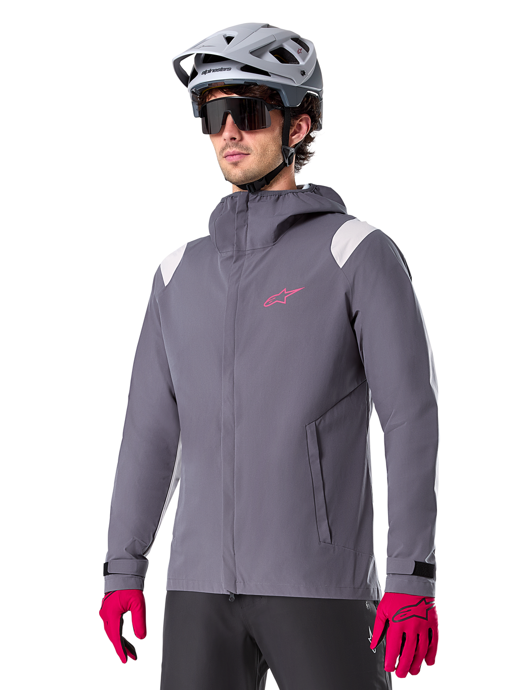 Alpinestars A-Dura Rain Jacket, chaqueta impermeable para ciclismo de montaña, gris titanio oscuro con logotipo rosa y acentos blancos en los hombros, diseño con capucha y bolsillos frontales, combinada con guantes rosas y casco de ciclismo gris claro