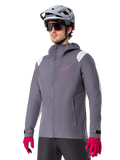 Alpinestars A-Dura Rain Jacket, chaqueta impermeable para ciclismo de montaña, gris titanio oscuro con logotipo rosa y acentos blancos en los hombros, diseño con capucha y bolsillos frontales, combinada con guantes rosas y casco de ciclismo gris claro