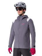 Alpinestars A-Dura Rain Jacket, chaqueta impermeable para ciclismo de montaña, gris titanio oscuro con logotipo rosa y acentos blancos en los hombros, diseño con capucha y bolsillos frontales, combinada con guantes rosas y casco de ciclismo gris claro