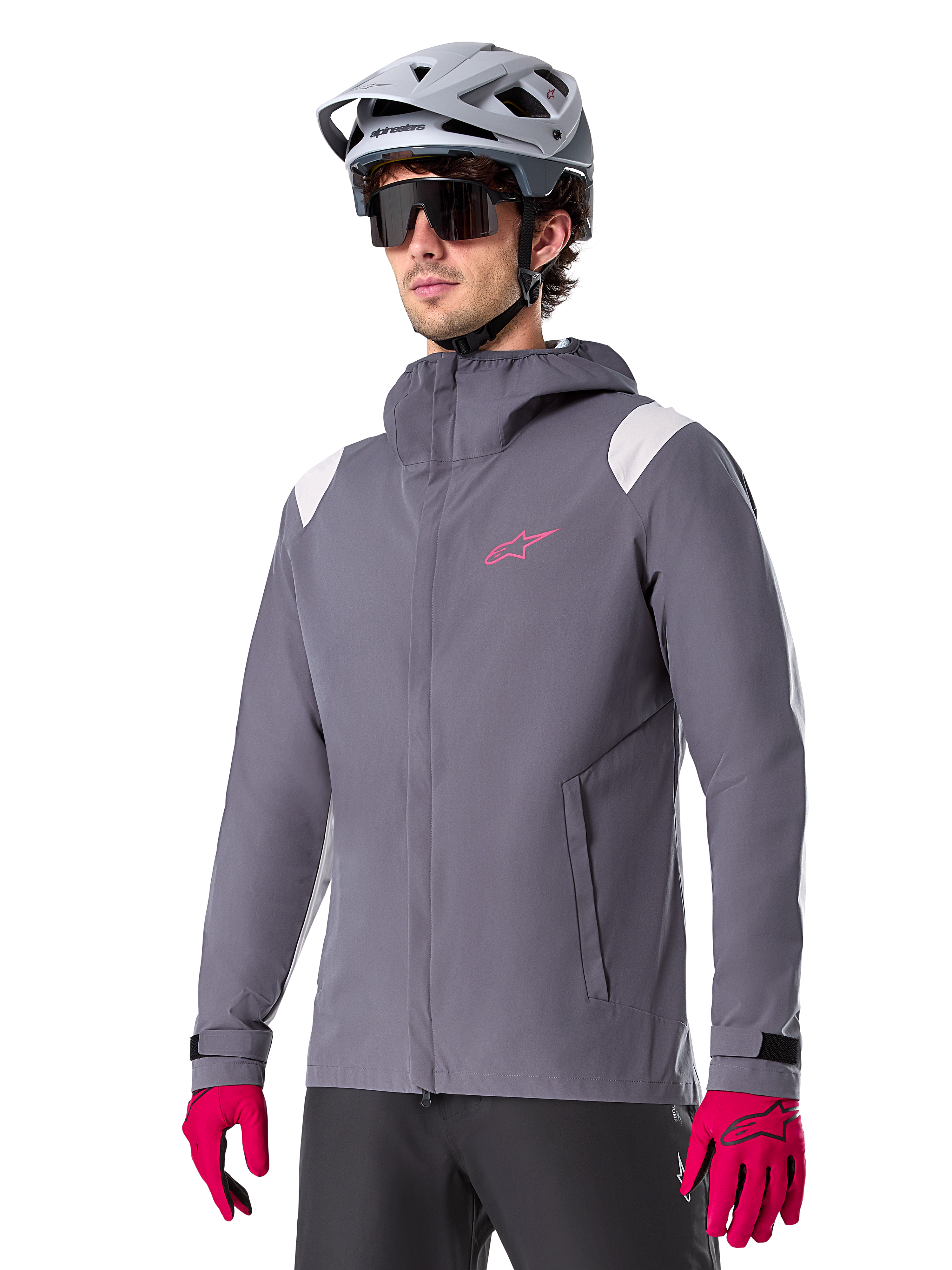 Alpinestars A-Dura Rain Jacket, chaqueta impermeable para ciclismo de montaña, gris titanio oscuro con logotipo rosa y acentos blancos en los hombros, diseño con capucha y bolsillos frontales, combinada con guantes rosas y casco de ciclismo gris claro