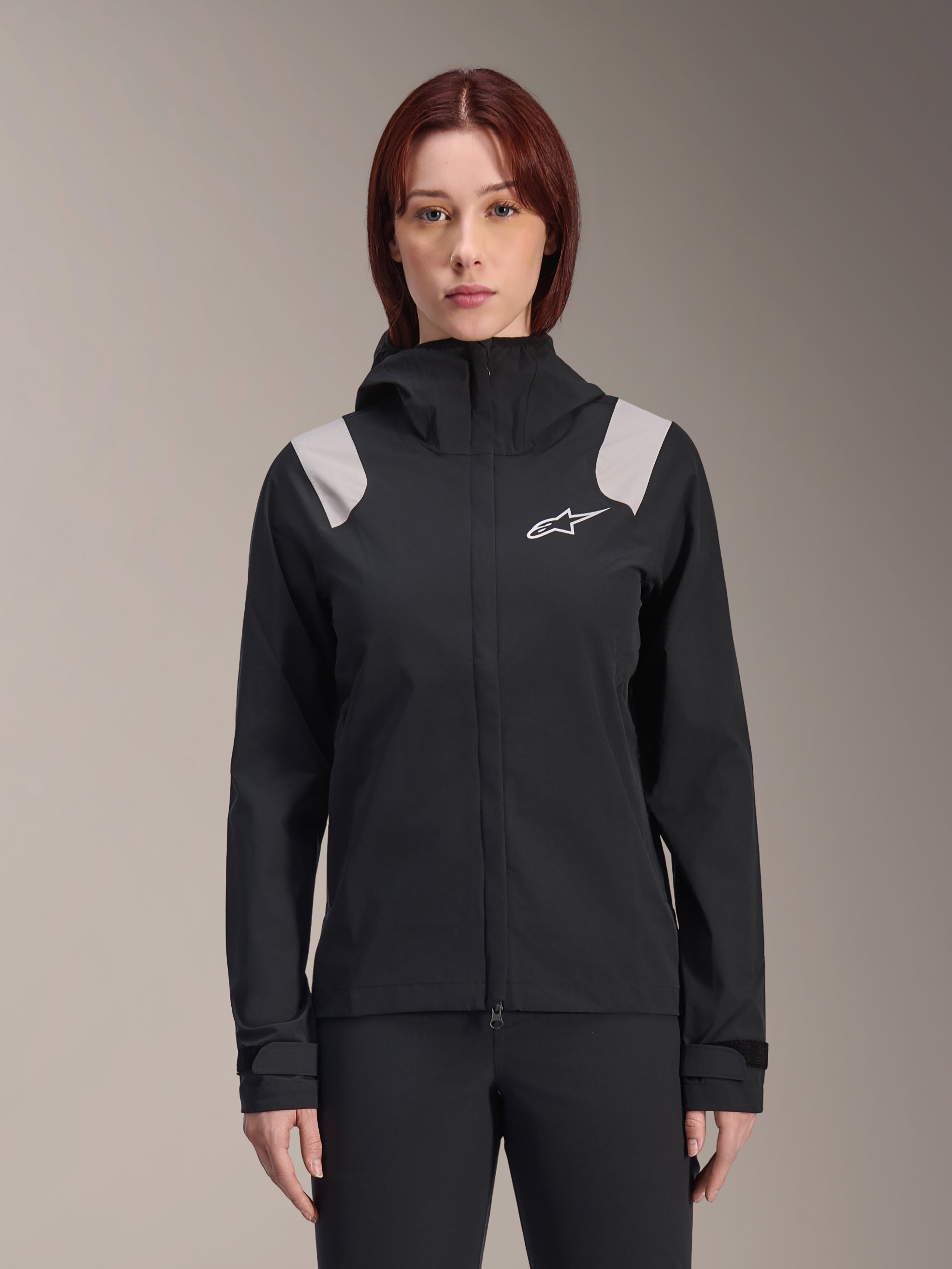 Alpinestars Stella A-Dura Rain Jacket, chaqueta impermeable de ciclismo para mujer, negra con paneles gris claro en los hombros, chaqueta técnica con capucha y logo blanco en el pecho, puños ajustables con velcro, equipamiento profesional para MTB y conducción en climas húmedos