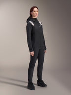 Mujer vistiendo la chaqueta de lluvia Alpinestars Stella A-Dura en color negro, capa exterior impermeable de 2.5 capas para MTB con detalles en gris claro en los hombros, pantalones negros y zapatillas de ciclismo a juego, retrato de estudio para equipamiento de ciclismo de alto rendimiento.