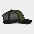 Gorra Snapback Flag de Alpinestars, verde militar y negro, vista de perfil lateral con visera curvada y paneles traseros de malla negra, parche rectangular frontal con logo blanco y rayas, accesorio casual inspirado en el automovilismo