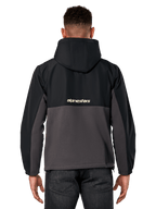 Chaqueta híbrida Alpinestars Juncture, vista posterior, negro y gunmetal, anorak deportivo casual de material mixto, parte superior de ripstop y parte inferior de forro polar de lona, logotipo de Alpinestars en la espalda, usado con pantalones oscuros
