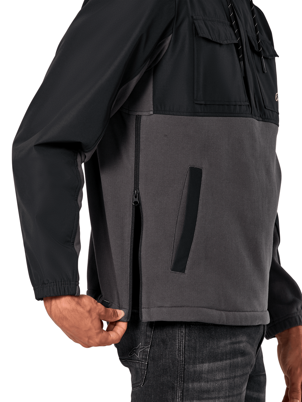Chaqueta Híbrida Juncture de Alpinestars en Black Gunmetal, vista de detalle lateral que destaca la cremallera lateral y el bolsillo inferior de ojal, diseño de materiales mixtos con forro polar de lona gris y capas de ripstop negro, ropa de calle casual inspirada en el automovilismo