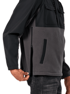 Chaqueta Híbrida Juncture de Alpinestars en Black Gunmetal, vista de detalle lateral que destaca la cremallera lateral y el bolsillo inferior de ojal, diseño de materiales mixtos con forro polar de lona gris y capas de ripstop negro, ropa de calle casual inspirada en el automovilismo