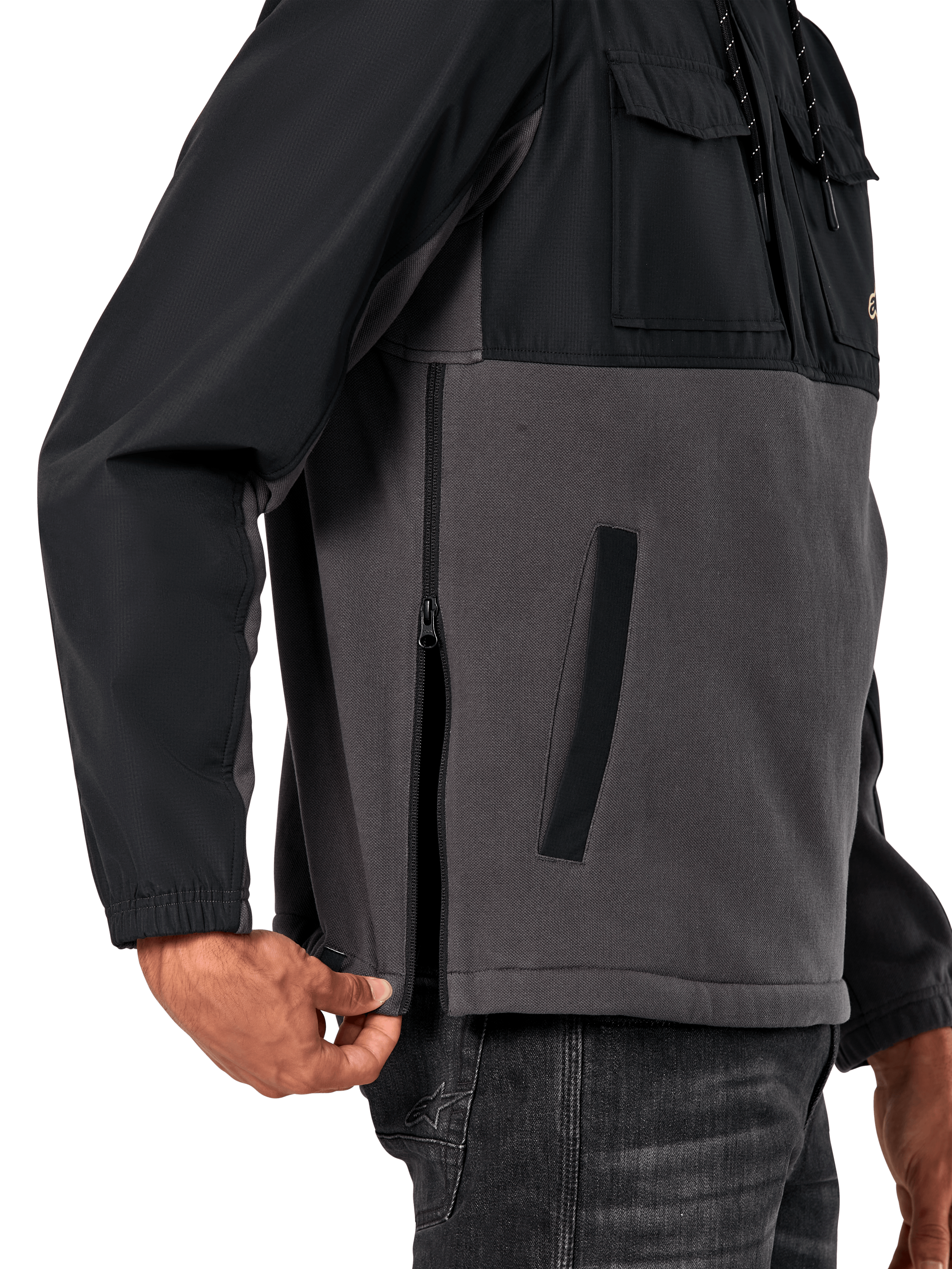 Chaqueta Híbrida Juncture de Alpinestars en Black Gunmetal, vista de detalle lateral que destaca la cremallera lateral y el bolsillo inferior de ojal, diseño de materiales mixtos con forro polar de lona gris y capas de ripstop negro, ropa de calle casual inspirada en el automovilismo