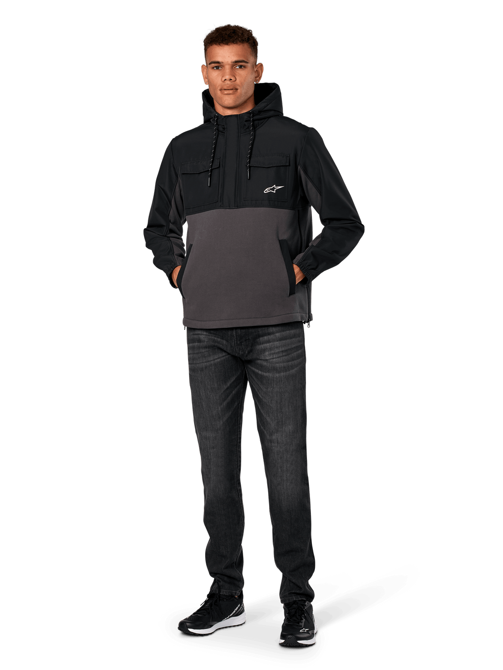 Chaqueta Híbrida Juncture de Alpinestars, negro y gris gunmetal, sudadera tipo anorak de material mixto con cuerpo de forro polar de lona y superposiciones de ripstop, logotipo A-star blanco en el pecho, capucha con cordón, lucida por un modelo con vaqueros oscuros y zapatillas negras, ropa urbana casual inspirada en el automovilismo