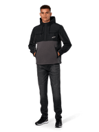 Chaqueta Híbrida Juncture de Alpinestars, negro y gris gunmetal, sudadera tipo anorak de material mixto con cuerpo de forro polar de lona y superposiciones de ripstop, logotipo A-star blanco en el pecho, capucha con cordón, lucida por un modelo con vaqueros oscuros y zapatillas negras, ropa urbana casual inspirada en el automovilismo