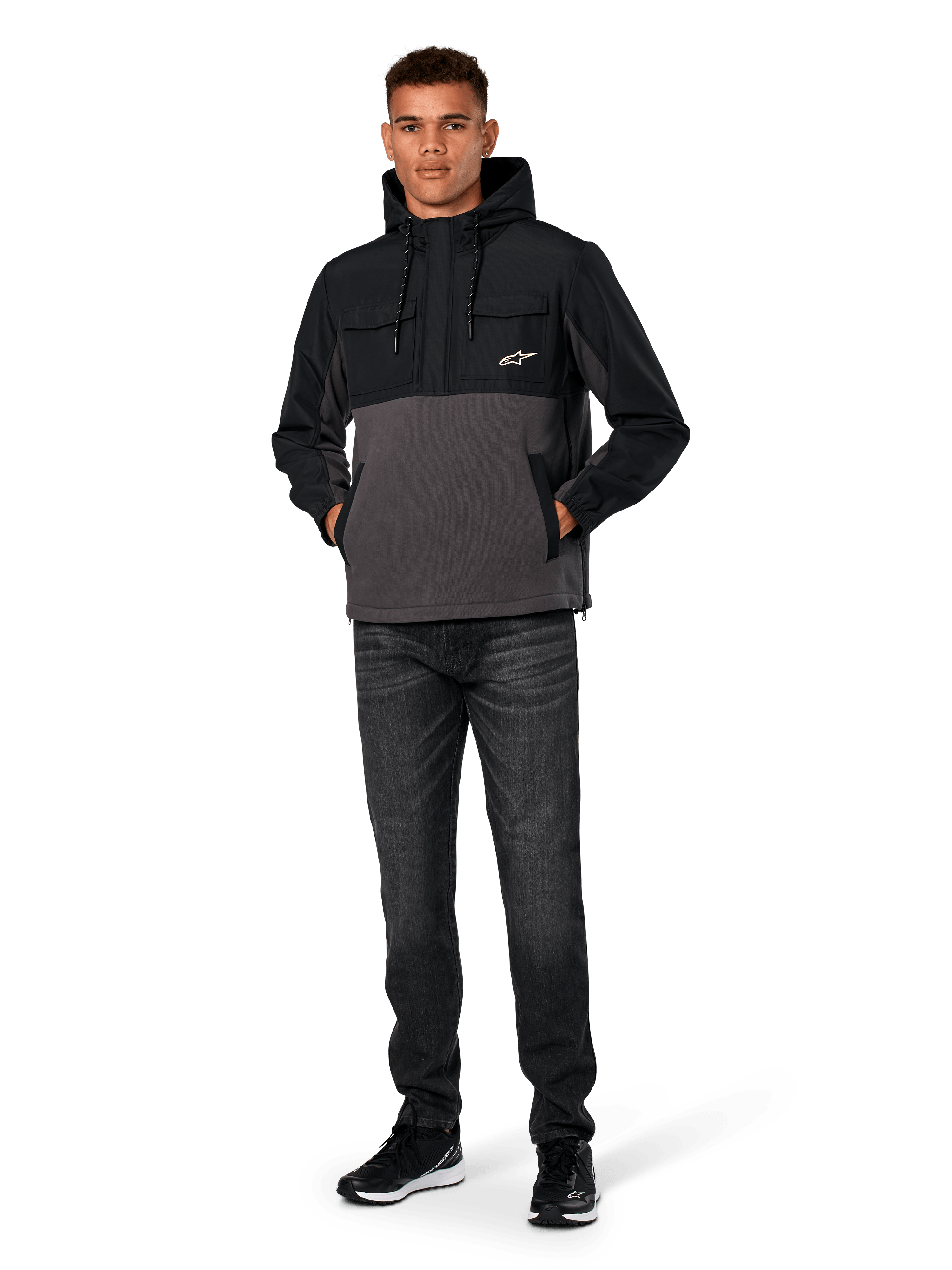 Chaqueta Híbrida Juncture de Alpinestars, negro y gris gunmetal, sudadera tipo anorak de material mixto con cuerpo de forro polar de lona y superposiciones de ripstop, logotipo A-star blanco en el pecho, capucha con cordón, lucida por un modelo con vaqueros oscuros y zapatillas negras, ropa urbana casual inspirada en el automovilismo