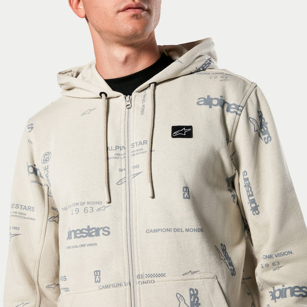 Alpinestars Plenitude Hoodie, sudadera con capucha y cremallera frontal en color Off White, estampado gráfico integral con texto 'alpinestars' y '1963', parche de logotipo negro bordado en el pecho, capucha con cordón, estilo streetwear de inspiración motorsport