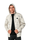 Sudadera con capucha Plenitude de Alpinestars, ropa deportiva casual, sudadera con cremallera frontal en blanco roto con gráficos de logotipos grises por toda la prenda, usada por un hombre con la capucha puesta sobre una camiseta negra, con un pequeño parche con el logotipo en el pecho y bolsillo tipo canguro