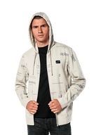 Sudadera con capucha Plenitude de Alpinestars, ropa deportiva casual, sudadera con cremallera frontal en blanco roto con gráficos de logotipos grises por toda la prenda, usada por un hombre con la capucha puesta sobre una camiseta negra, con un pequeño parche con el logotipo en el pecho y bolsillo tipo canguro