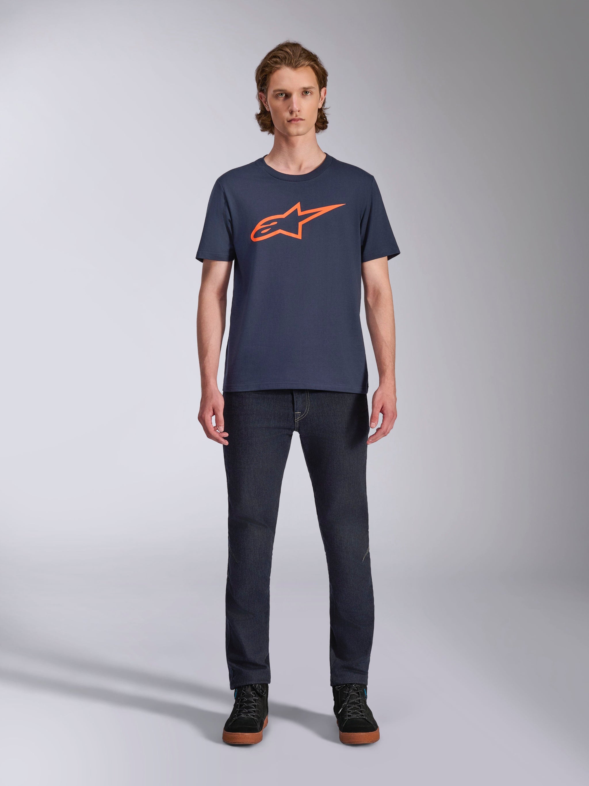 Alpinestars Ageless 2.0 CSF Tee, camiseta de manga corta, azul marino con el logotipo de Alpinestars en naranja, lucida por un modelo con vaqueros oscuros y zapatillas, ropa urbana casual de estilo motorsport