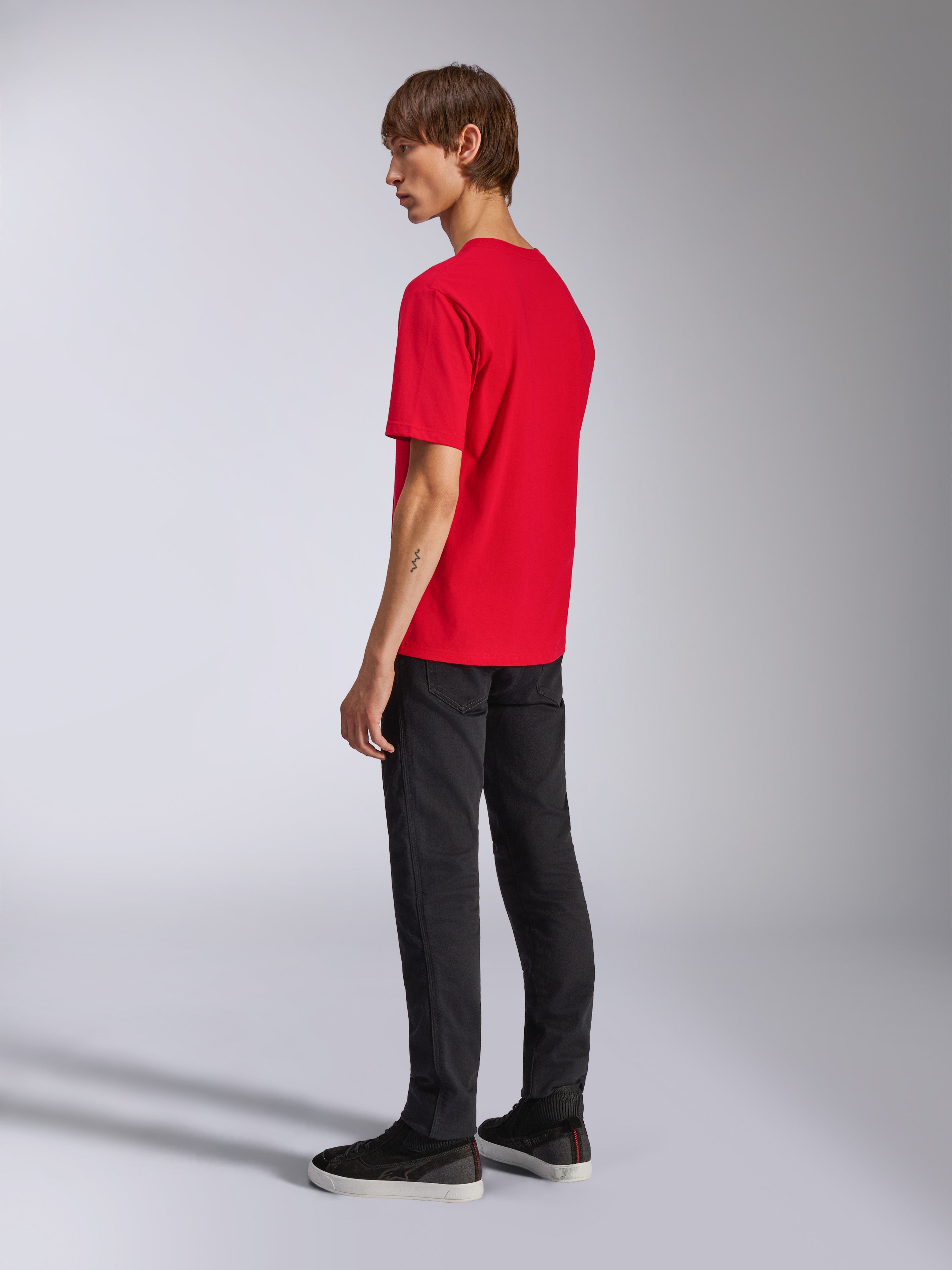 Alpinestars Ageless Shadow CSF Tee, camiseta de manga corta, roja, vista trasera en modelo, usada con pantalones negros y zapatillas, ropa urbana casual inspirada en el automovilismo
