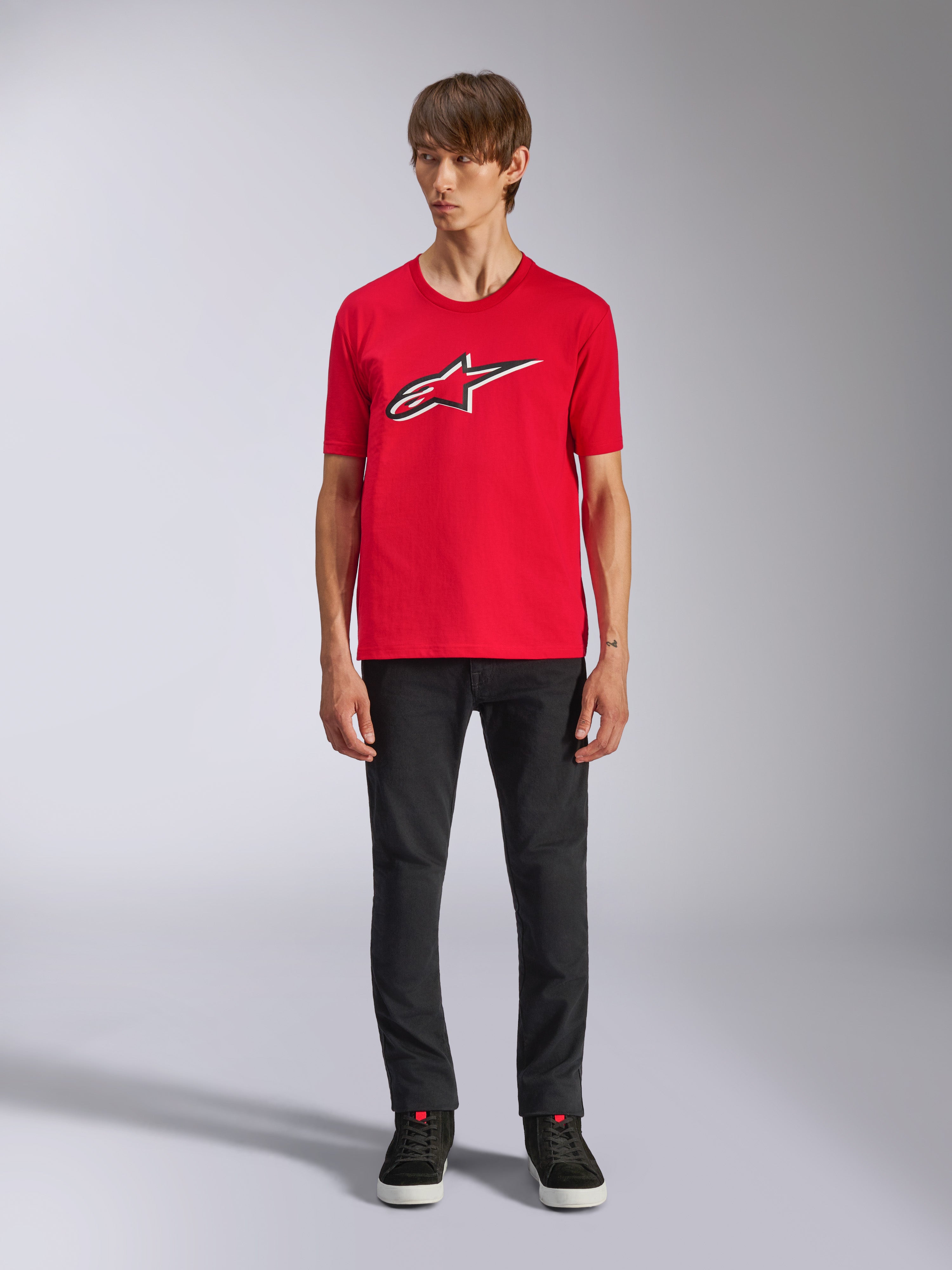 Camiseta Alpinestars Ageless Shadow CSF, camiseta de manga corta, roja, logo Ageless frontal con contornos blancos y negros, usada por un modelo con pantalones negros y zapatillas, ropa urbana casual de automovilismo