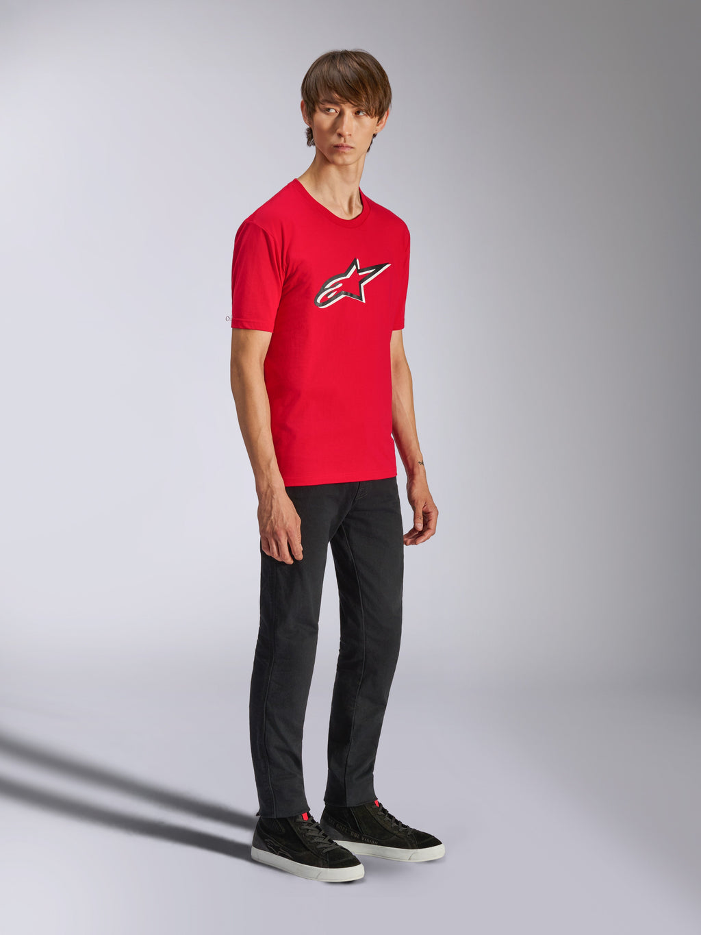 Alpinestars Ageless Shadow CSF Tee, camiseta de manga corta roja, con un gran logotipo Ageless en el pecho, usada por un modelo con pantalones negros y zapatillas, estilo streetwear casual de automovilismo