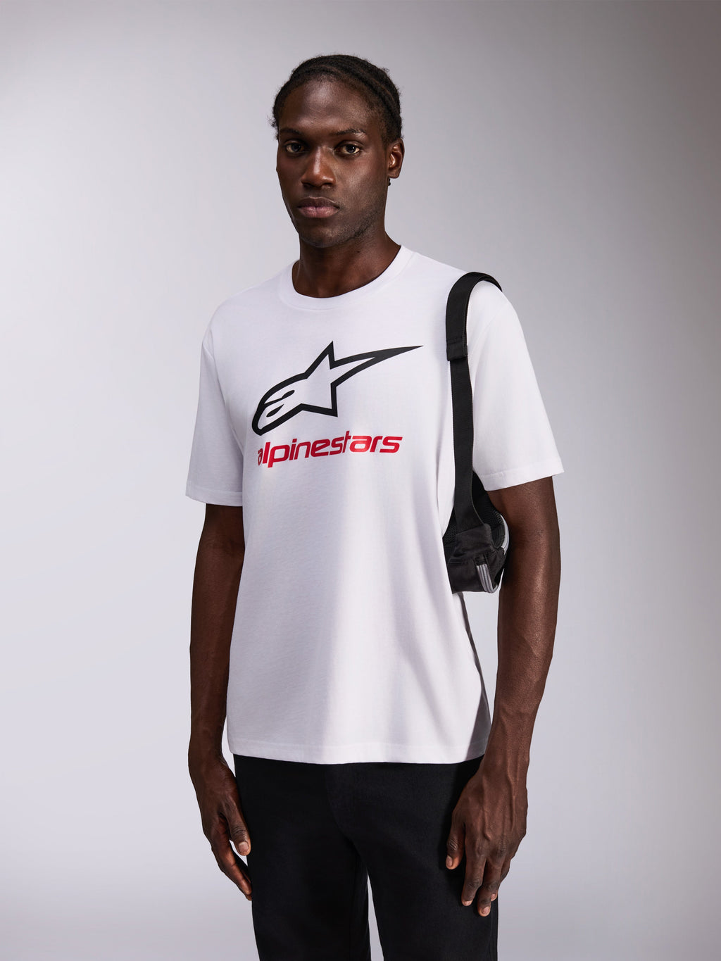 Alpinestars Always 2.0 CSF Tee, Short Sleeve T-Shirt, White with large Black Star Logo and Red branding, worn by model with black pants and shoulder bag, casual motorsport-inspired streetwear