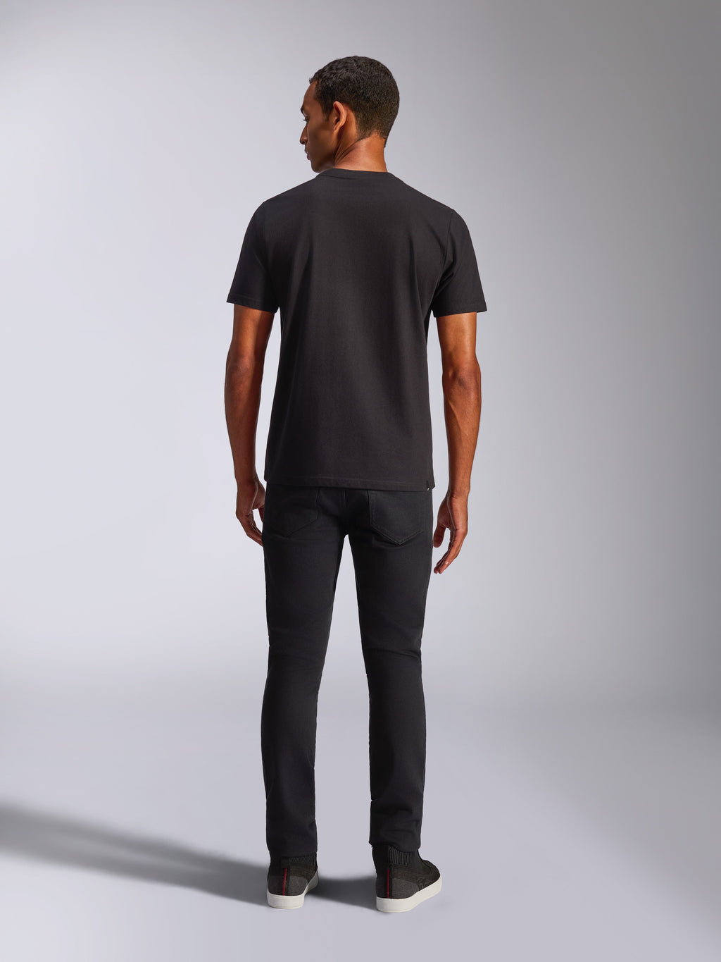 Camiseta Alpinestars Blaze 2.0 CSF, camiseta de manga corta, negra, vista posterior, combinada con vaqueros negros, ropa urbana informal inspirada en el automovilismo