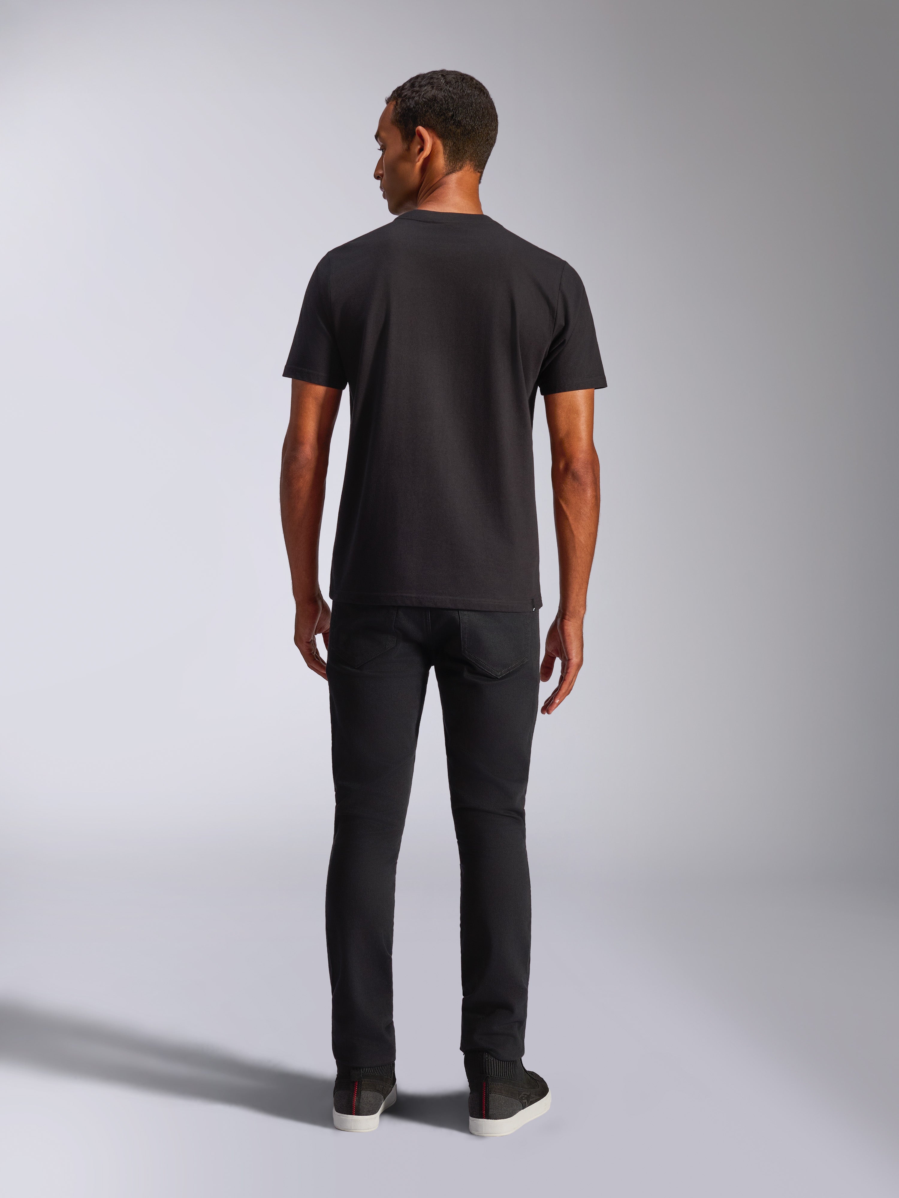 Camiseta Alpinestars Blaze 2.0 CSF, camiseta de manga corta, negra, vista posterior, combinada con vaqueros negros, ropa urbana informal inspirada en el automovilismo