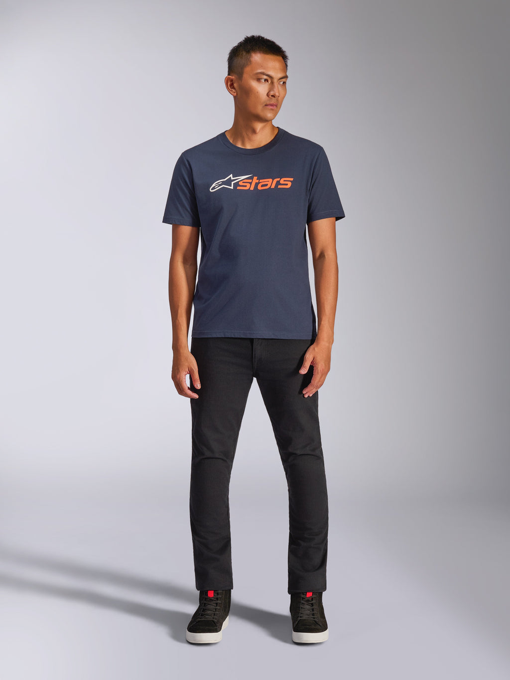 Camiseta Alpinestars Blaze 2.0 CSF, camiseta de manga corta, azul marino con el logotipo de Astars en blanco y naranja, combinada con pantalones negros y zapatillas negras, ropa urbana casual inspirada en el automovilismo