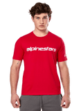 Alpinestars Linear Wordmark 2.0 CSF Tee, camiseta de manga corta roja, marca de palabra lineal blanca en el pecho y logotipo Ageless en la manga, lucida por un modelo masculino con pantalones de chándal grises, estilo urbano casual inspirado en el automovilismo