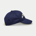 Alpinestars Par Hat, gorra de béisbol azul marino, vista lateral que muestra el bordado del logotipo en blanco y amarillo, visera curva con borde tipo sándwich amarillo, accesorio casual con corona estructurada