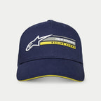 Gorra Par de Alpinestars, azul marino, gorra estructurada tipo snapback con visera curva, con logotipo Astars 3D blanco y gráfico 'alpinestars RACING AHEAD' en gris y amarillo, detalle de visera tipo sándwich amarilla, estilo urbano casual inspirado en el motor