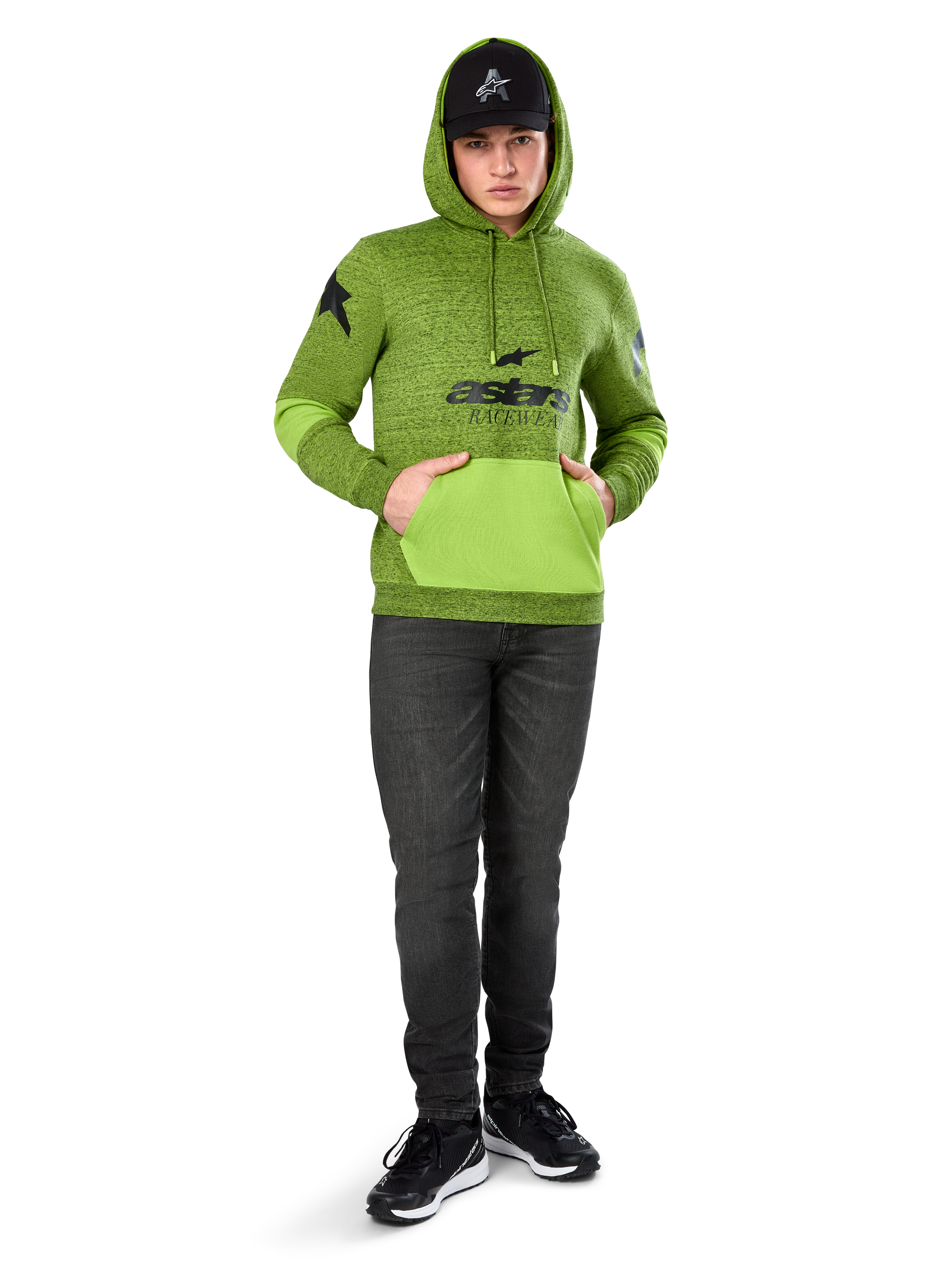 Alpinestars Perpetuate Hoodie, sudadera de forro polar jaspeado verde lima con bolsillo canguro y paneles en las mangas en verde brillante a contraste, gráfico frontal 'astars' en negro, combinada con gorra negra y vaqueros oscuros, ropa urbana casual inspirada en el motorsport