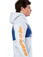Sudadera con capucha Alpinestars Specter, estilo urbano casual, blanca con estampado de degradado azul, logotipo de Alpinestars en naranja de gran tamaño en la manga, perfil lateral de un hombre usando la sudadera