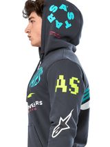 Alpinestars Variegate Hoodie, sudadera de forro polar gris plomo con cremallera frontal, perfil lateral del modelo, diseño con múltiples logotipos en amarillo neón, azul claro y blanco, incluye marca 'AS' en la manga y 'STARS' en la capucha, ropa urbana casual inspirada en el automovilismo