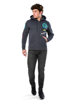 Alpinestars Variegate Hoodie, sudadera de forro polar con cremallera frontal, gris Gunmetal, usada por un modelo con vaqueros negros y zapatillas, con la marca 'ASTARS' en color turquesa y logotipos coloridos en las mangas y el pecho, ropa urbana casual de inspiración motorsport