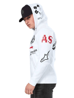 Sudadera con capucha Alpinestars Variegate, sudadera de forro polar blanca con cremallera frontal, diseño de múltiples logotipos en las mangas y la capucha con letras 'AS' en rojo y logotipo de estrella en negro, usada por un hombre con gorra negra, estilo casual motorsport streetwear