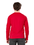 Vista trasera de un hombre con la camiseta de manga larga Alpinestars Committed CSF en color rojo, combinada con vaqueros gris oscuro, con el logotipo de Alpinestars visible en blanco en la manga y un diseño minimalista en la espalda.