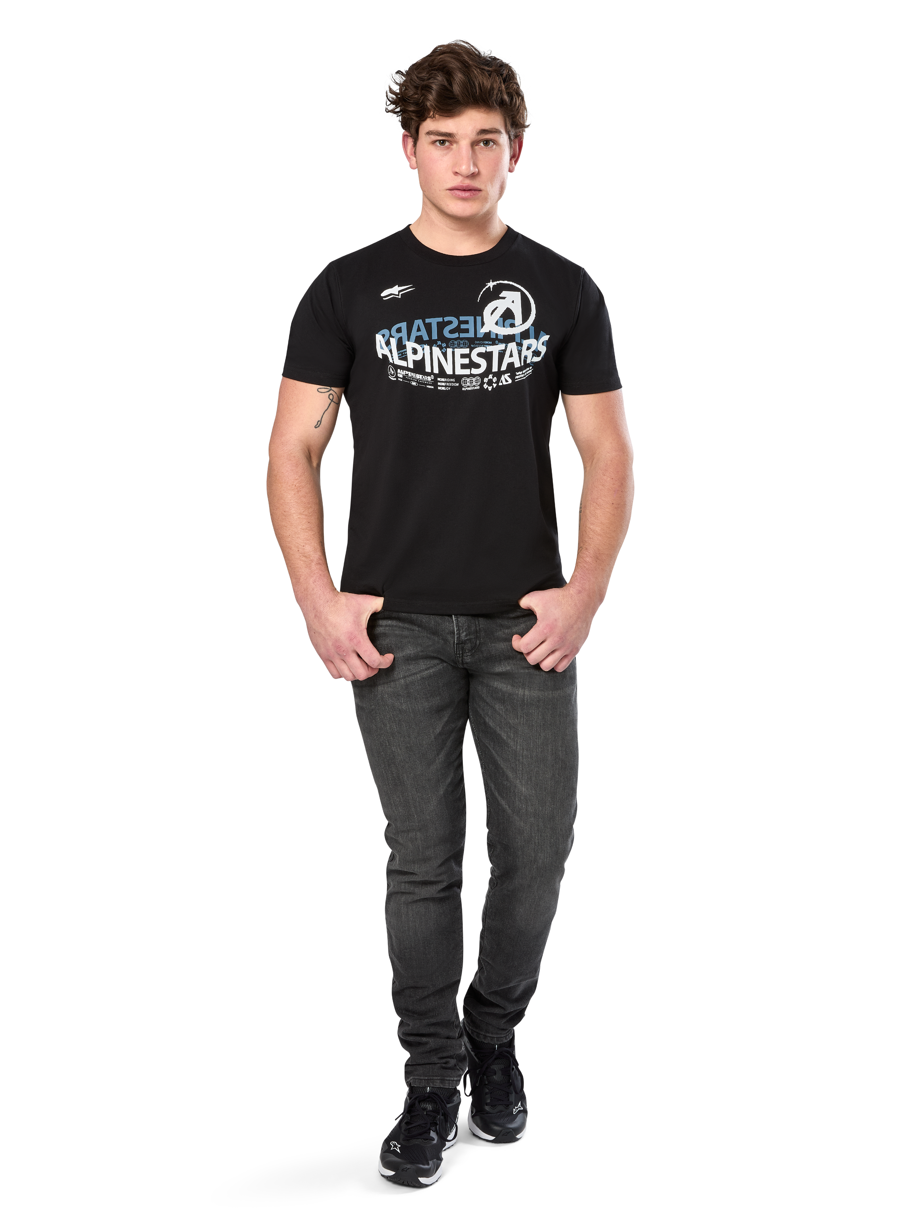 Alpinestars Semicircle CSF Tee, camiseta de manga corta, negra, gráfico curvado en blanco y azul claro en el pecho, usada por un modelo con vaqueros gris oscuro y zapatillas negras, ropa urbana casual de estilo motor