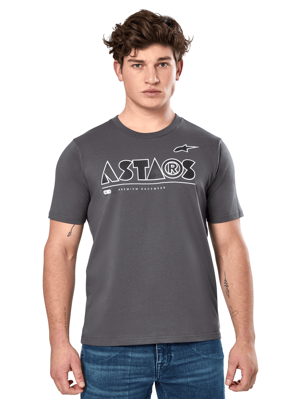 Alpinestars Cereal CSF Tee, camiseta de manga corta gris carbón, lucida por un modelo masculino con vaqueros azules, logotipo geométrico ASTARS blanco y texto 'Premium Racewear', ropa casual de estilo de vida inspirada en el automovilismo