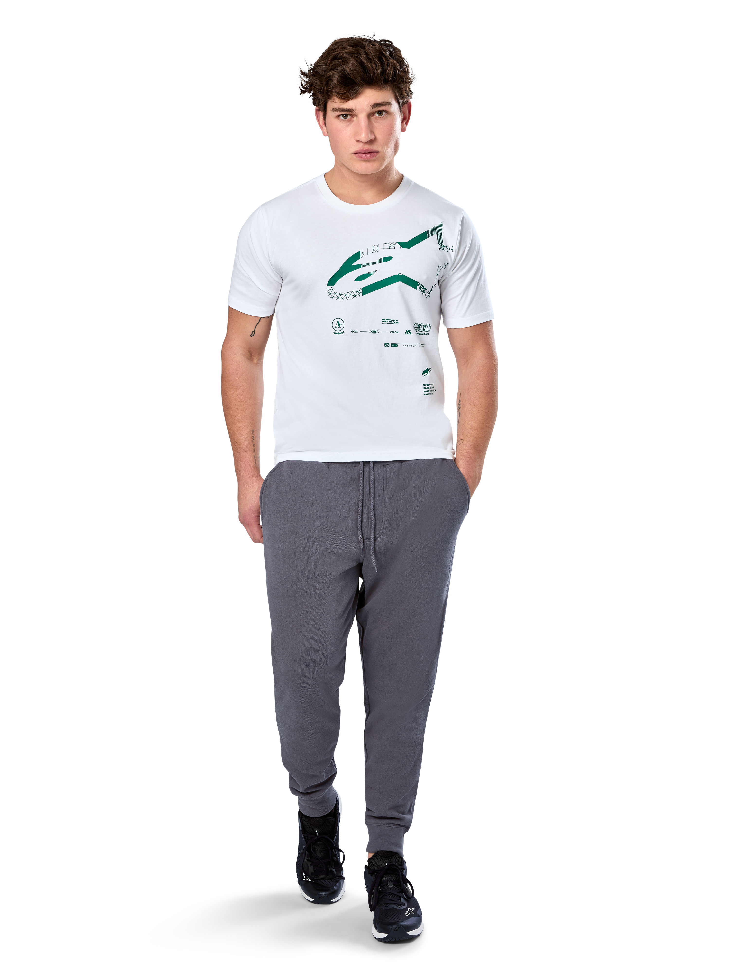 Alpinestars Geografica CSF Tee, camiseta de manga corta, blanca, logotipo Astars verde con gráfico multi-tech geográfico, combinada con pantalones de chándal grises y zapatillas negras, estilo casual de ropa urbana de automovilismo