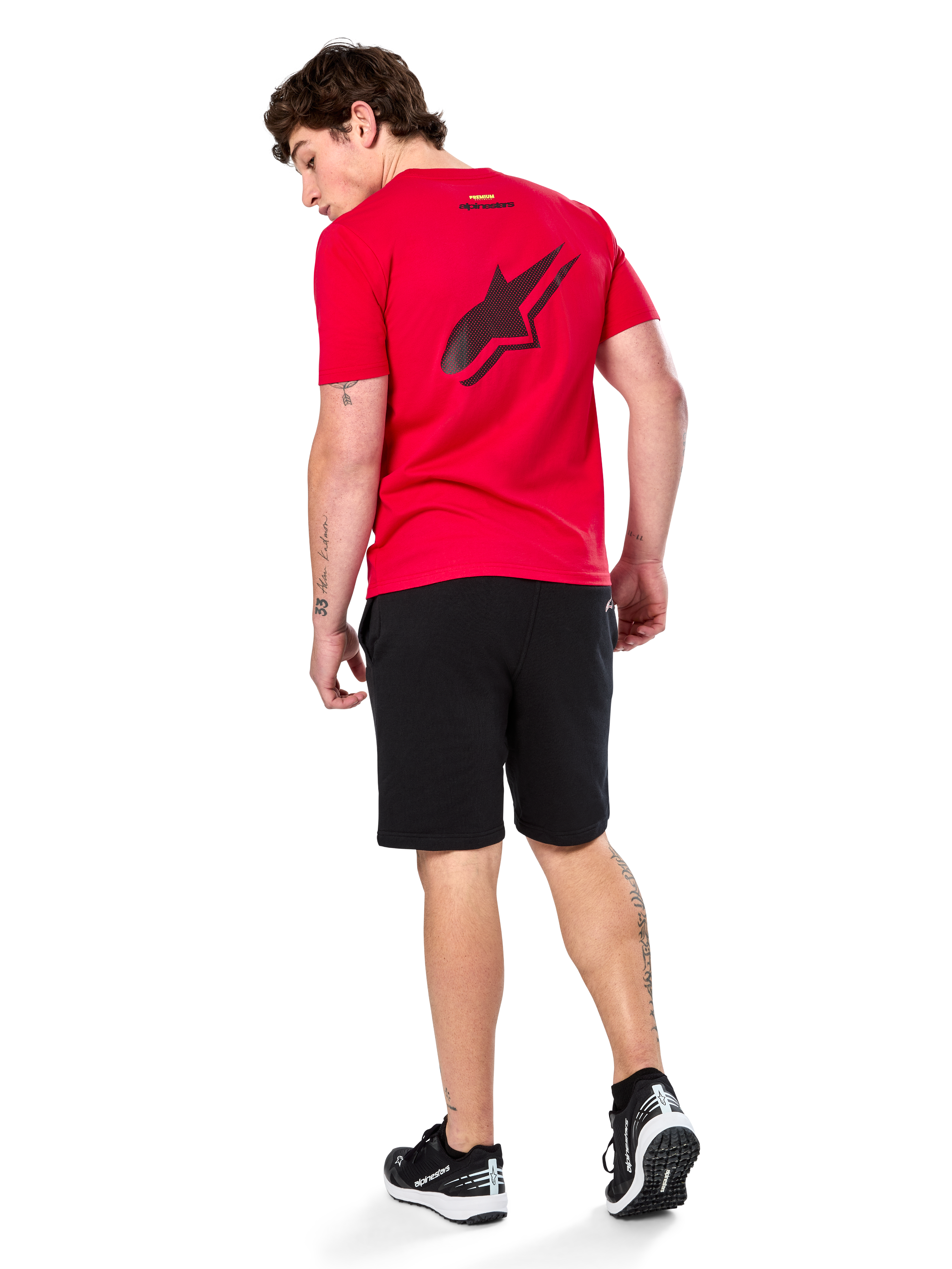 Camiseta Alpinestars Formulate CSF, camiseta de manga corta, roja, logotipo grande de Astars perforado en negro en la espalda, combinada con pantalones cortos negros y zapatillas, ropa urbana informal inspirada en el mundo del motor