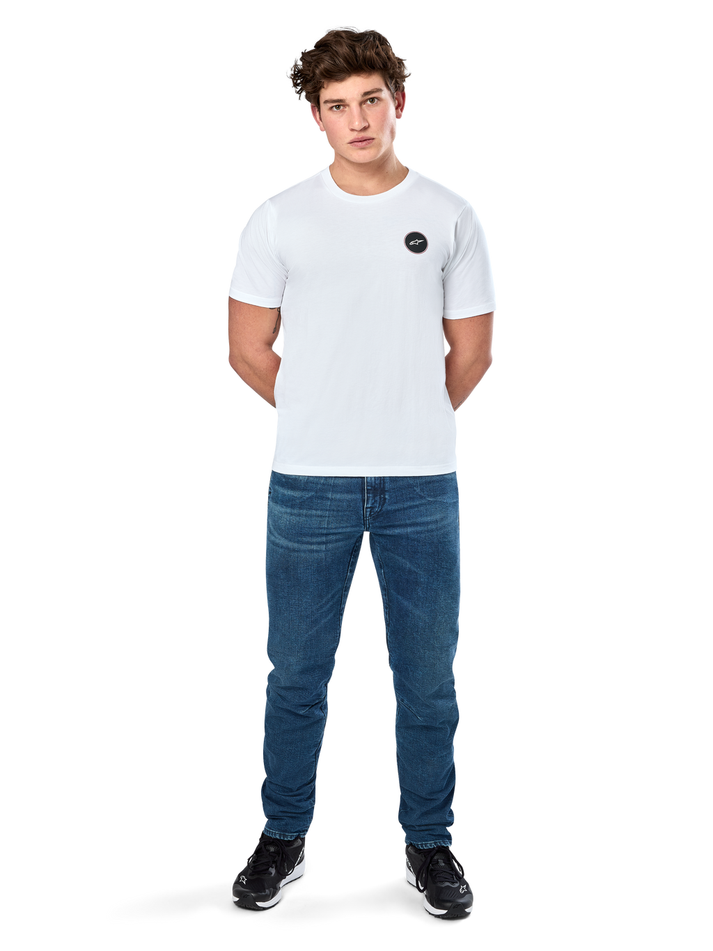 Alpinestars Dot Carbon Csf Tee, camiseta de manga corta, blanca, logotipo circular Astars con efecto de fibra de carbono, ropa casual de estilo automovilismo, usada por un modelo masculino con pantalones vaqueros azules y zapatillas negras