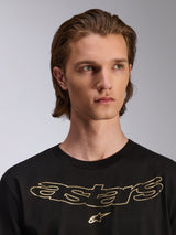 Camiseta Alpinestars Luxo CSF de manga corta, color negro, con logotipo de Astars en el pecho en dorado metálico, lucida por un modelo masculino, diseño casual de inspiración motorsport