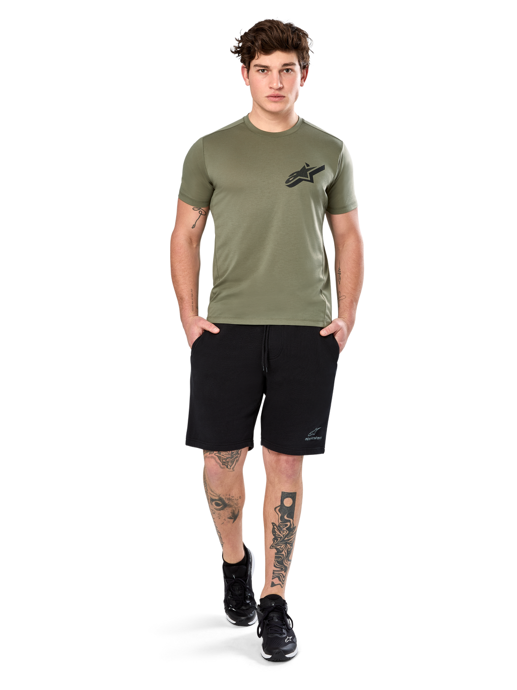 Alpinestars Attrition Performance Tee, camiseta de manga corta, verde claro, con un logotipo Astars negro en el pecho, combinada con pantalones cortos deportivos negros y zapatillas negras, imagen de estilo de vida con ropa deportiva casual de alto rendimiento