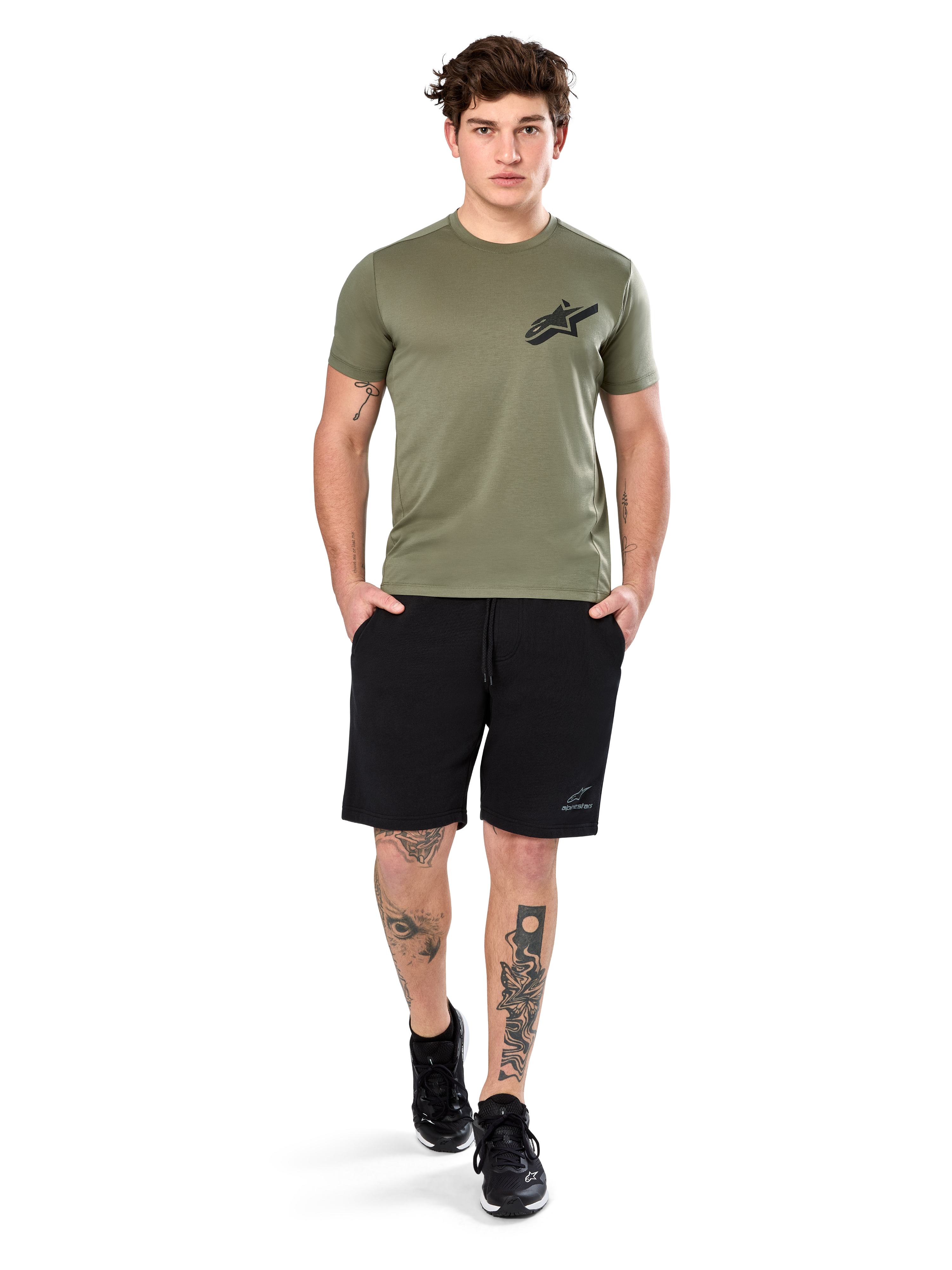 Alpinestars Attrition Performance Tee, camiseta de manga corta, verde claro, con un logotipo Astars negro en el pecho, combinada con pantalones cortos deportivos negros y zapatillas negras, imagen de estilo de vida con ropa deportiva casual de alto rendimiento