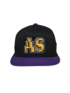 Alpinestars Franchise Hat, gorra de visera plana en negro y morado, corona estructurada con visera y botón superior morados, con un logotipo "AS" bordado en 3D en color dorado en el frente, estilo casual de moda urbana inspirado en el automovilismo