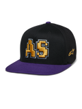 Alpinestars Franchise Hat, gorra de visera plana en negro y morado, logo AS bordado en 3D en dorado con contorno blanco, visera y botón superior morados, diseño estructurado Flex Fit