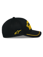 Gorra Luminary de Alpinestars, gorra snapback negra, vista lateral, visera curva con ribete de sutache amarillo, logotipo bordado en 3D y estrella lateral amarillos, 100% sarga de algodón, accesorio casual inspirado en el automovilismo