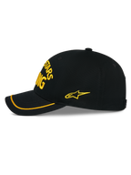 Gorra Luminary de Alpinestars, gorra snapback negra vista desde el lateral, bordado amarillo en 3D en el frente y el lateral, visera curva con ribete de sutache amarillo, construcción estructurada de sarga de algodón