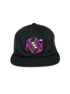 Gorra Alpinestars That Way Trucker, gorra trucker negra, incluye un parche gráfico en color púrpura y negro con el texto 'One Vision One Goal', visera plana, corona estructurada y paneles traseros de malla, prenda de cabeza casual inspirada en el automovilismo