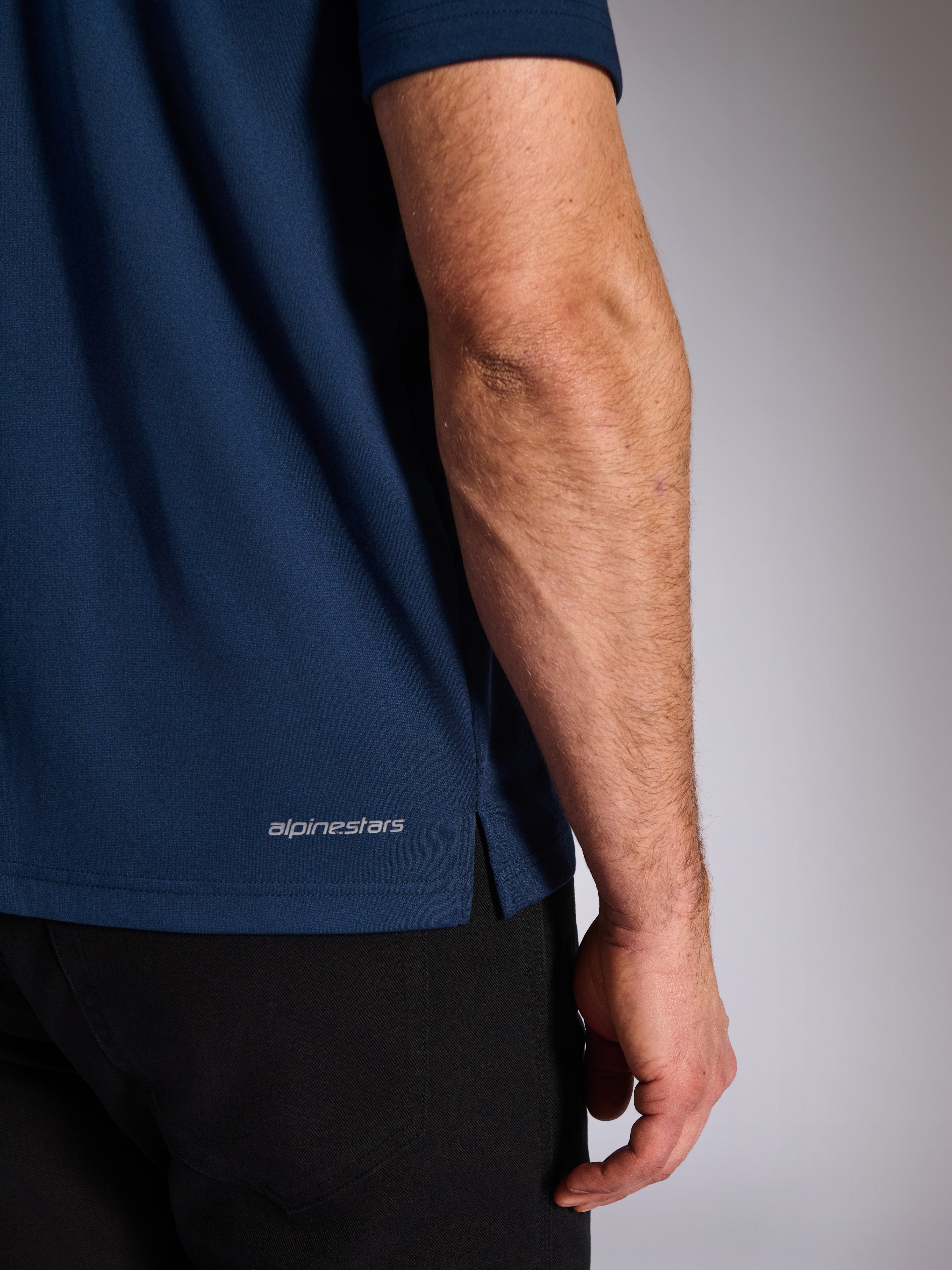 Alpinestars Impetus Sport Polo, Navy, Close-up of the lower hem showing the Alpinestars wordmark and side vent, mock-mesh knit texture, casual motorsport sportswear