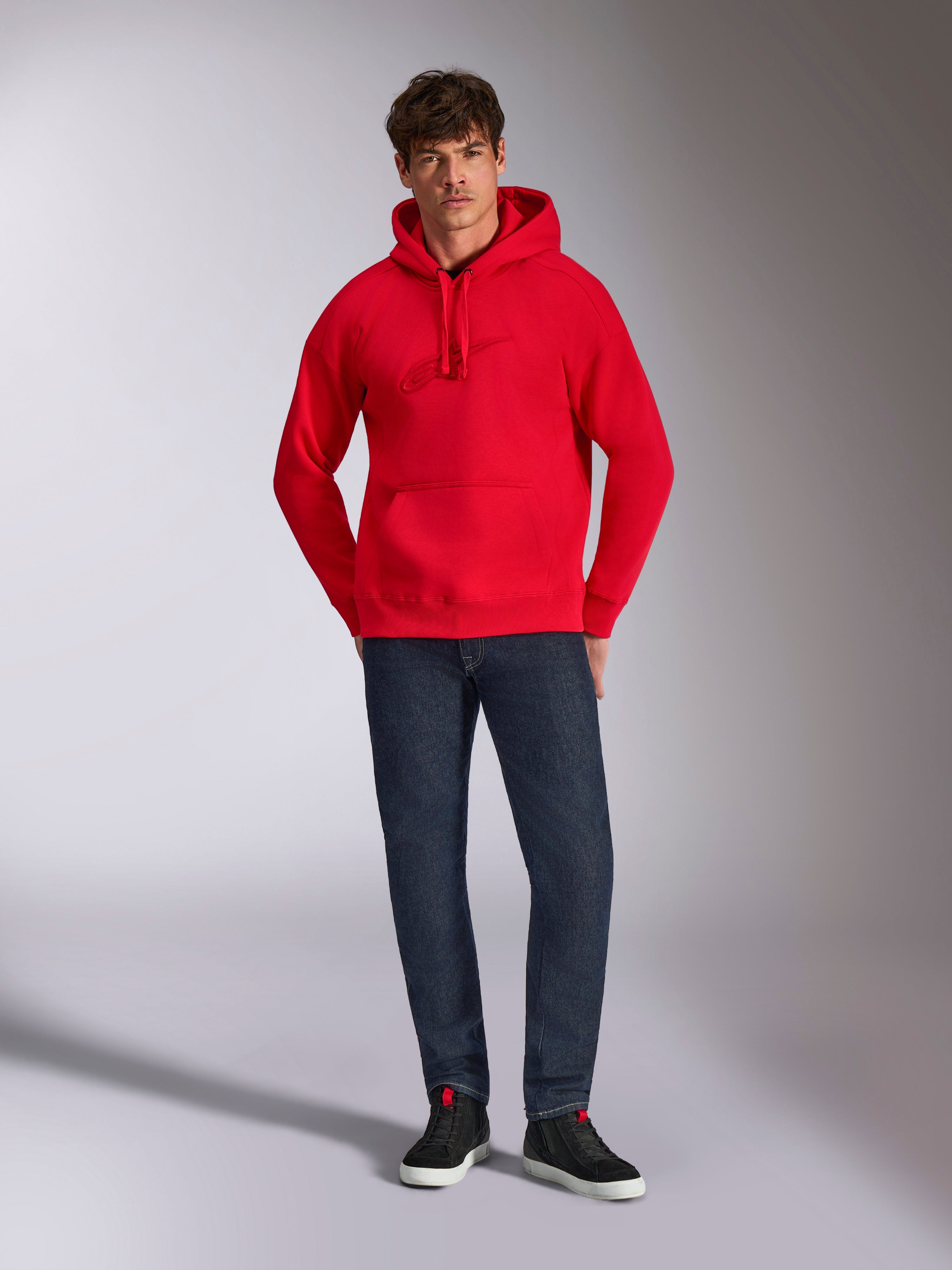 Alpinestars Emergent Oversized Hoodie, Red, featuring tonal 3D embroidered Astars logo on the chest, kangaroo pocket and drawstring hood, worn by a model with dark blue jeans and black sneakers, casual lifestyle streetwear